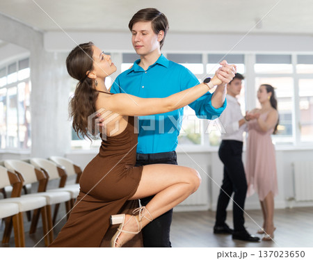 Girl and guy in festive clothes dancing slow ballroom dance during group lesson in choreography studio Girl and guy in festive clothes dancing slow ballroom dance during group lesson in choreography studio 137023650