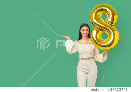 A young woman smiles while holding a large gold number 8 balloon A young woman smiles while holding a large gold number 8 balloon 137023741