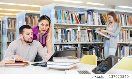 Woman and man looking at laptop screen together in library Woman and man looking at laptop screen together in library 137023840