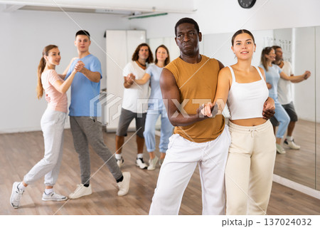 Class of positive multinational couples enjoing partner pair dancing during class together in modern dance hall Class of positive multinational couples enjoing partner pair dancing during class together in modern dance hall 137024032