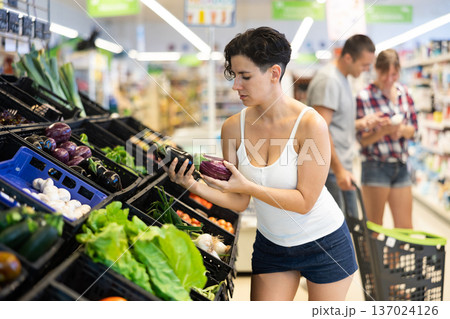 Latin american young female shopper choosing eggplants in store Latin american young female shopper choosing eggplants in store 137024126