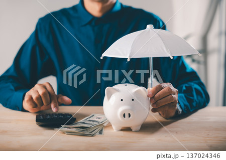 Piggy bank money protect financial insurance concept risk umbrella collage finance illustrates wealth security, while person uses calculator near cash stack on wooden office desk 137024346