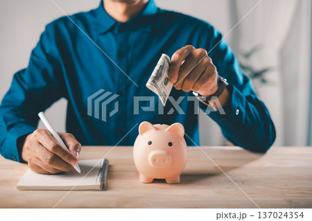 piggy bank, learning for education, saving for college, career growth, person inserts dollar into piggy bank while writing in notebook, plans budget for student tuition and success 137024354