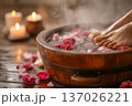 Relaxing foot spa scene with female feet over wooden bowl of water, rose petals, steam. Professional pedicure wellness concept in dim candle light. Traditional herbal therapy, relaxation, copy-space. 137026221