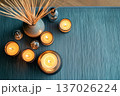 A top-view spa composition shows a blue textured yoga mat with several burning candles and an incense reed diffuser, illustrating a mindful meditation practice and spiritual wellness at home. 137026224