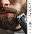 Extreme close-up of young man trimming thick brown beard with professional electric clipper. Detailed male grooming concept. Facial hair maintenance, barbering, daily hygiene. Macro texture stubble. 137026232