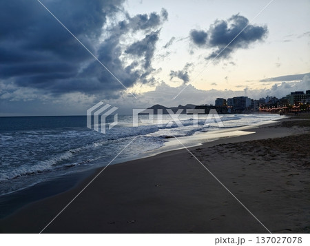 Somber dusk over pacific beach scene, Stormy evening cast across sandy coast with cloudy skies Somber dusk over pacific beach scene, Stormy evening cast across sandy coast with cloudy skies 137027078