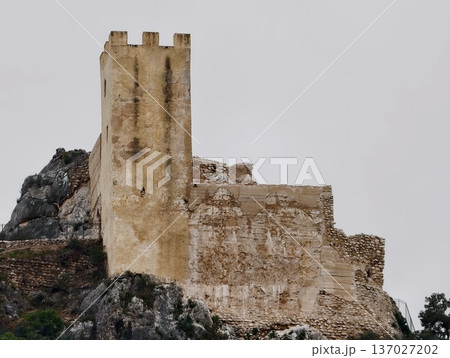 Historical fortress built on rough terrain, Ancient defensive structure perched over jagged stone base 137027202