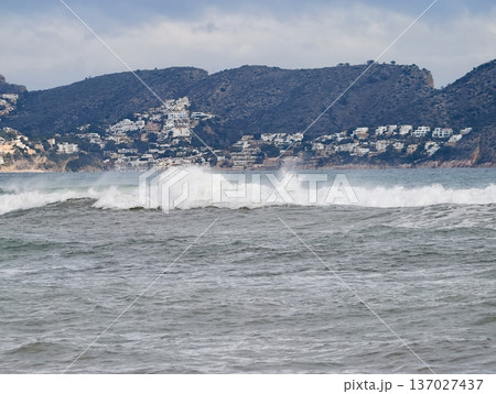Wild sea crashes on coastal terrain, Aggressive waves strike rugged shoreline near resort buildings 137027437