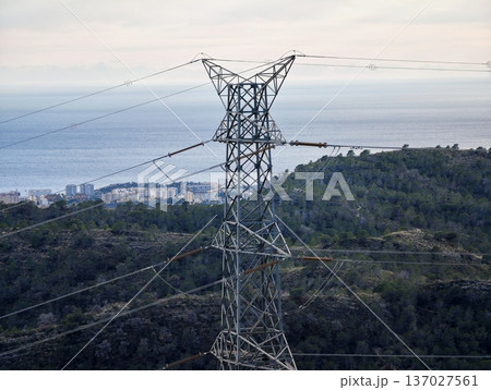 High voltage transmission on coast, Electrical transmission tower spanning landscape with distant town 137027561
