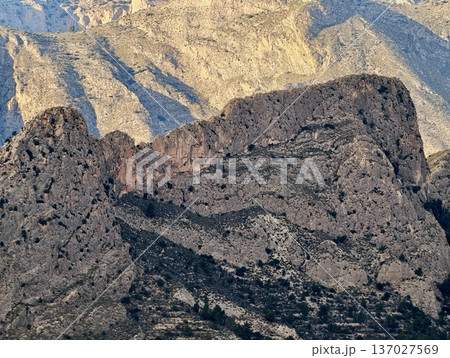 Textured mountain ridgeline showcasing layered sedimentary formations and minimal vegetation presence Textured mountain ridgeline showcasing layered sedimentary formations and minimal vegetation presence 137027569