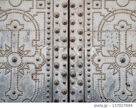 Ornamental metal door with rivets, Weathered metal door featuring rivets and embedded floral patterns Ornamental metal door with rivets, Weathered metal door featuring rivets and embedded floral patterns 137027694