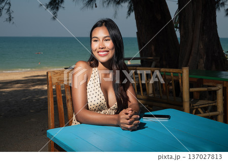 Smiling Woman Sitting at Beachside Cafe Table 137027813