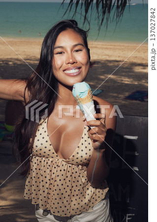 Close-up portrait of smiling woman holding melting ice cream on sunny beach Close-up portrait of smiling woman holding melting ice cream on sunny beach 137027842