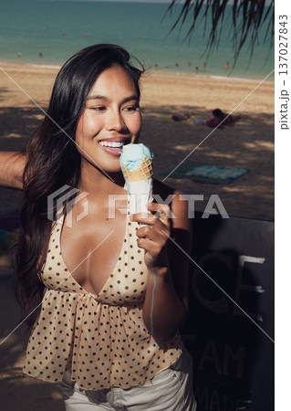 Close-up portrait of smiling woman holding melting ice cream on sunny beach Close-up portrait of smiling woman holding melting ice cream on sunny beach 137027843
