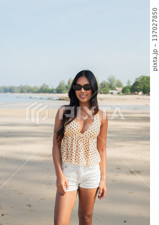 Smiling Young Asian Thai Woman Standing on Beach in Summer Outfit Wearing Sunglasses Smiling Young Asian Thai Woman Standing on Beach in Summer Outfit Wearing Sunglasses 137027850