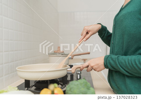 Person Cooking in Modern Kitchen Preparing Healthy Meal with Fresh Vegetables and Attention to Detail Using Wooden Spoon and Non-Stick Pan Person Cooking in Modern Kitchen Preparing Healthy Meal with Fresh Vegetables and Attention to Detail Using Wooden Spoon and Non-Stick Pan 137028323