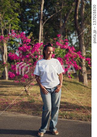 Smiling Mature Woman Standing in Tropical Garden with Pink Flowers 137028830