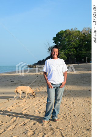 Mature woman standing on tropical beach wearing 90s style normcore fashion jeans and white t-shirt Mature woman standing on tropical beach wearing 90s style normcore fashion jeans and white t-shirt 137028867