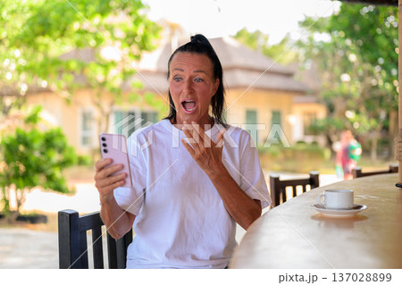Surprised Senior Woman Reading Message on Smartphone at Outdoor Cafe Surprised Senior Woman Reading Message on Smartphone at Outdoor Cafe 137028899