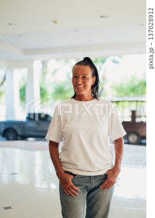 Smiling senior woman standing in a bright open interior with natural light during summer Smiling senior woman standing in a bright open interior with natural light during summer 137028912