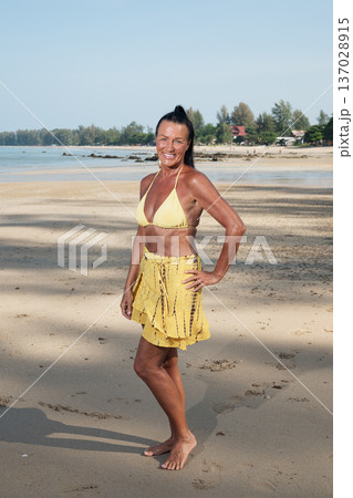 Fit Mature Woman in Yellow Bikini Standing on Tropical Beach 137028915
