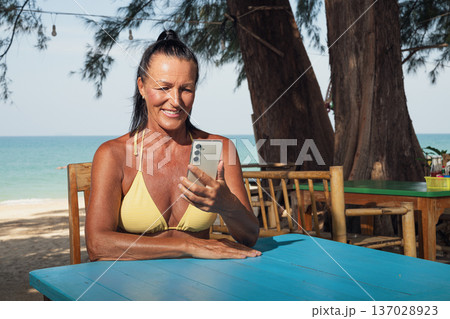 Smiling Fit Senior Woman Using Smartphone at Beach Cafe Smiling Fit Senior Woman Using Smartphone at Beach Cafe 137028923