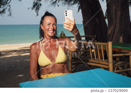 Fit Senior Woman Taking Selfie at Tropical Beach Cafe 137029000