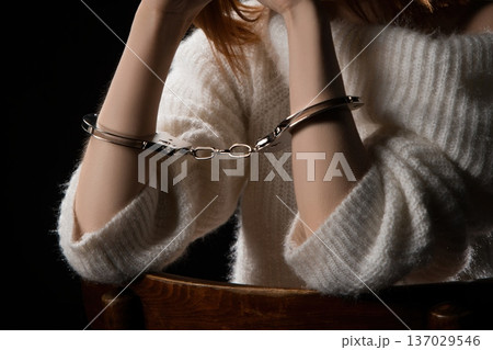 Hands in handcuffs resting on a wooden table with dim lighting 137029546