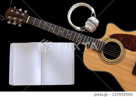 Classical acoustic guitar, headphones and notebook on a black background. 137030500