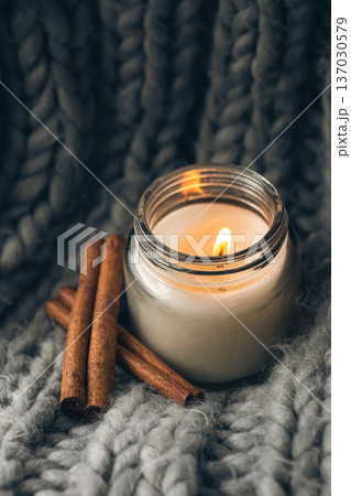 Close-up, candle and cinnamon sticks on the background of a gray knitted element. Close-up, candle and cinnamon sticks on the background of a gray knitted element. 137030579