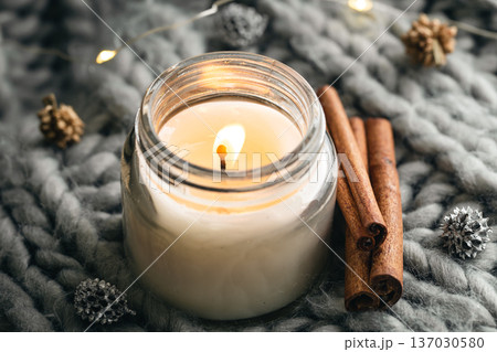 Close-up, candle and cinnamon sticks on the background of a gray knitted element. Close-up, candle and cinnamon sticks on the background of a gray knitted element. 137030580