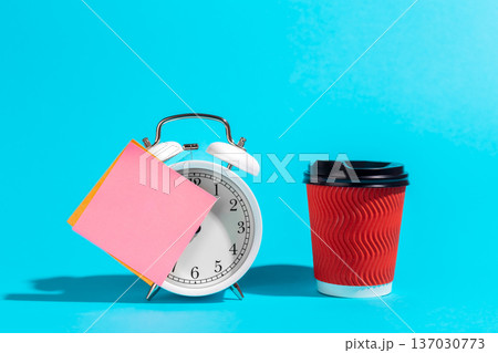 Alarm clock, cup and a blank pink sticker on a blue background. Alarm clock, cup and a blank pink sticker on a blue background. 137030773