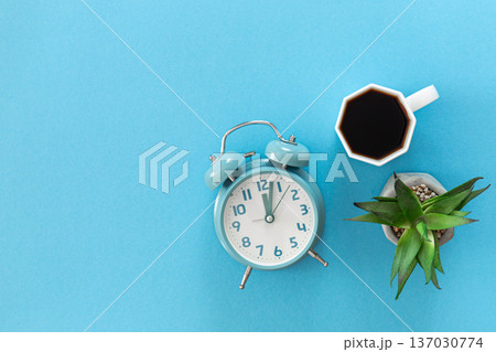 Alarm clock and a cup of coffee on a blue background, flat lay. Alarm clock and a cup of coffee on a blue background, flat lay. 137030774
