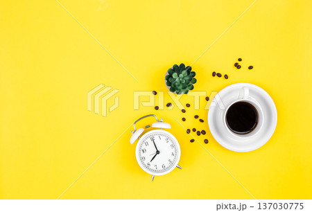 Alarm clock, cup of coffee and coffee beans on a yellow background, flat lay. Alarm clock, cup of coffee and coffee beans on a yellow background, flat lay. 137030775
