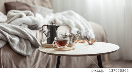 A cup of tea and a teapot on a blurred background of the interior of the room. A cup of tea and a teapot on a blurred background of the interior of the room. 137030863
