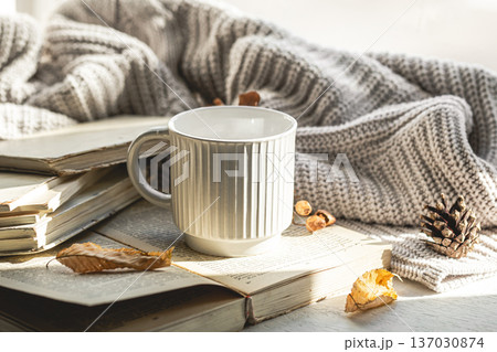 Autumn composition with a textured cup and a book on the windowsill. Autumn composition with a textured cup and a book on the windowsill. 137030874