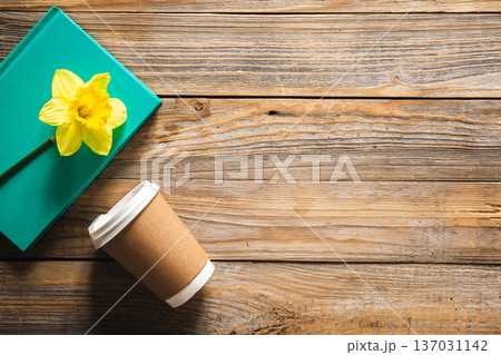 Book, paper disposable cup and yellow narcissus flower on wooden background. 137031142