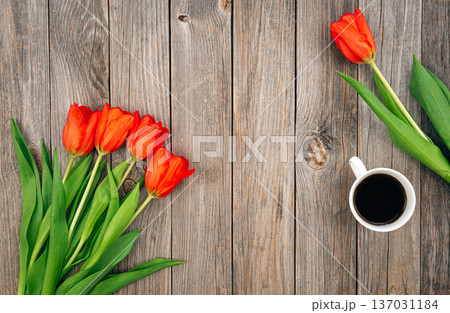Bouquet of red tulips and a cup of coffee on a wooden background, top view. 137031184