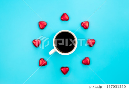 Chocolate sweets in the form of hearts and a cup of coffee on a blue background. Chocolate sweets in the form of hearts and a cup of coffee on a blue background. 137031320