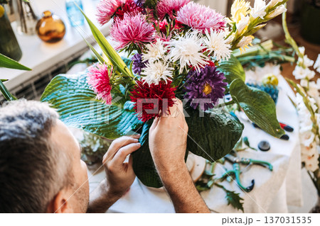 man arrange aster flowers and large green leaves in vintage vase. Stress management for men, therapeutic floristry, cortisol reduction, mindful craftsmanship, male wellness. man arrange aster flowers and large green leaves in vintage vase. Stress management for men, therapeutic floristry, cortisol reduction, mindful craftsmanship, male wellness. 137031535