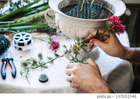 Person trims pink aster stem with garden shears over table with floral tools. ethical floristry, domestic flower industry, farm-to-vase, sustainable flower consumption. 137031546