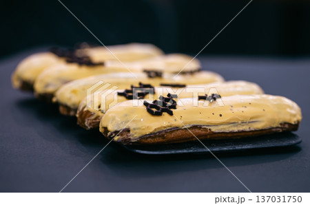 Close-up of eclairs in yellow glaze on a black background. Close-up of eclairs in yellow glaze on a black background. 137031750