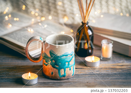 Cozy composition with a cup on a blurred background with books and bokeh lights. 137032203
