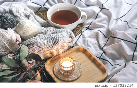 Cozy composition with a cup of tea, a candle and knitted elements on a blanket. Cozy composition with a cup of tea, a candle and knitted elements on a blanket. 137032214