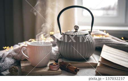 Cozy composition with a teapot, a cup and a book on a blurred background. Cozy composition with a teapot, a cup and a book on a blurred background. 137032237