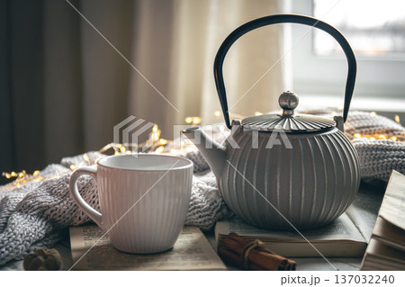 Cozy composition with a teapot, a cup and a book on a blurred background. Cozy composition with a teapot, a cup and a book on a blurred background. 137032240