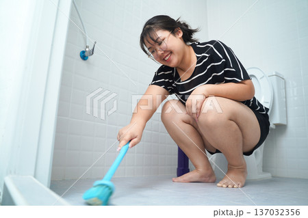 Happy young Asian woman scrubbing bathroom floor with a brush. 137032356