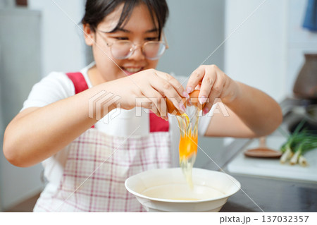 Young Asian woman cracking an egg into a bowl in the kitchen. 137032357