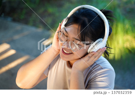 Happy young Asian woman wearing headphones and listening to music. Happy young Asian woman wearing headphones and listening to music. 137032359